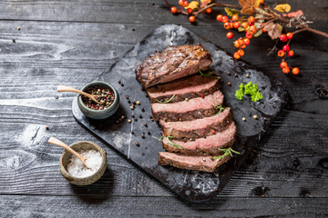 Sliced grilled roast beef with salt and pepper on marble plate on wooden old rustic table Black background. 