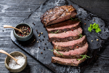 Sliced grilled roast beef with salt and pepper on marble plate on wooden old rustic table Black...