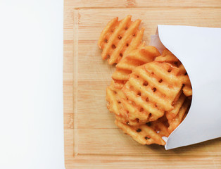 Criss Cut Fries in Take Away White Box on Wooden Board Plate. Fast Food meal freshly made from natural potatoes isolated with empty copy space top view. Unhealthy eating, take out, fast food concept