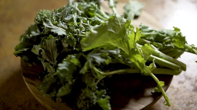 Clusters of stalks of fresh rapini on a round cutting board rotating in beautiful backlit light. Shallow depth of field.