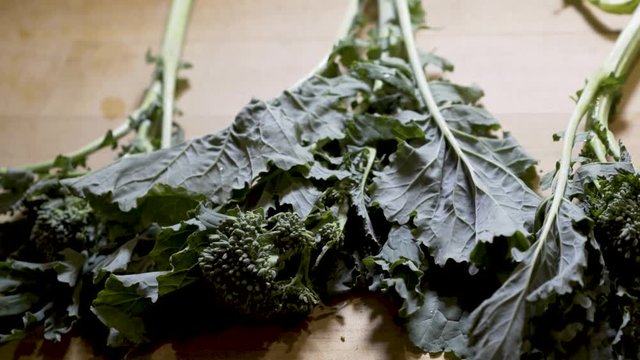Fresh stalks of rapini on a wood cutting board. Slide from right to left.