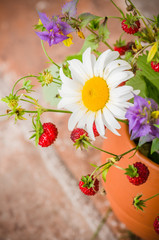 Ripe strawberries and a bouquet of forest flowers in a clay mug