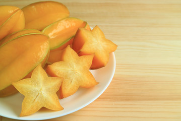 Plate of orange yellow ripe whole fruits and sliced Star Fruit served on wooden table, with free space for text and design 