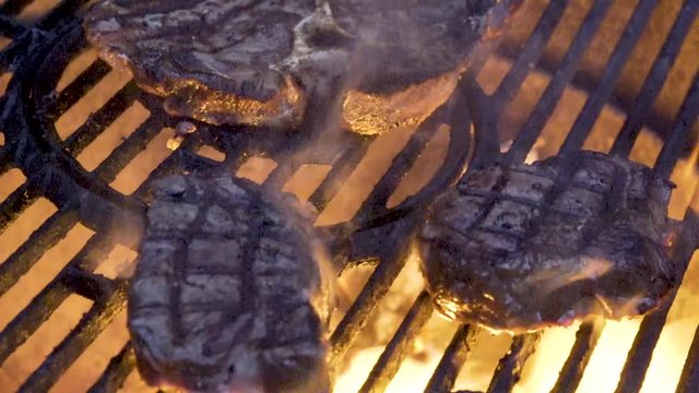 Closeup of two large pieces of filet mignon on the grill with flames licking at them and nice grill marks on the top as camera slides from left to right.