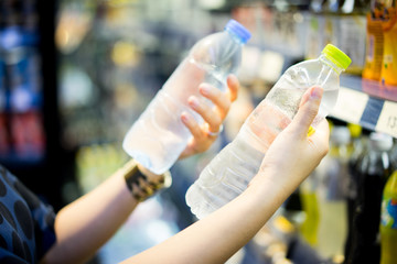 woman choosing cold bottle of water or beverage on shelves in supermarket store.