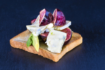 Frische Avocado, Feigen und Blauschimmelkaese auf Toastbrot als Vorspeise auf schwarzem Grund