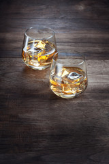 close up view of two glasses with ice and whiskey on wooden background