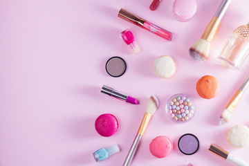 Make up products and macaroons border on pink background