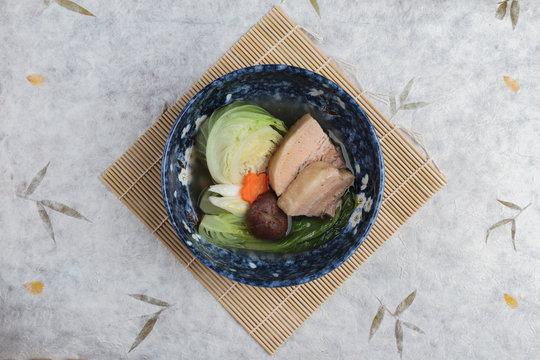 Top view of Pressure cooker pork belly (Kakuni) with cabbage, Japanese scallion, shiitake, carrot served in blue ceramic bowl on makisu (meal mat).