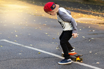 Little urban boy with a penny skateboard. Young kid riding in the park on a skateboard. City style. Urban kids.