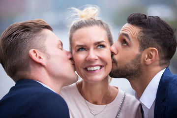 two young men kissing woman on her cheeks