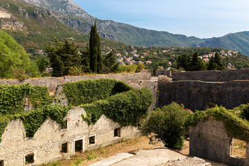 Fototapeta na wymiar Herceg Novi, Montenegro. Stone houses and walls covered by ivy and oleander. Mountains and town in the background.