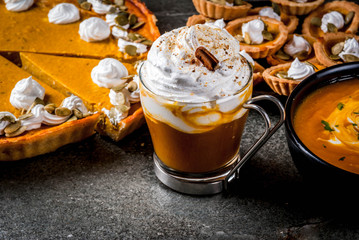 Set of traditional autumn food. Halloween, Thanksgiving. Spicy pumpkin latte, pumpkin pie and tartalets with whipped cream and pumpkin seeds, pumpkin soup, on black stone table. Copy space