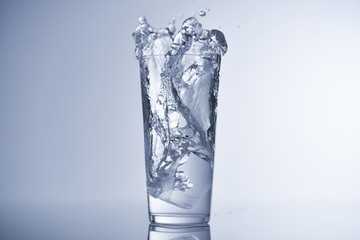 Ice cube falling into glass of water