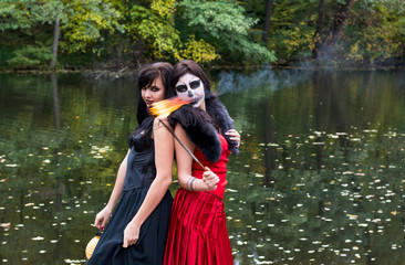 Two brunettes women with makeup like a Halloween skull and Halloween witch makeup stands with a...