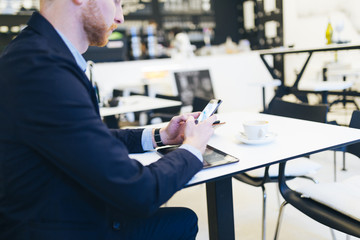 Young confident redhead business man looking something at his mobile phone. Selective focus on hand.