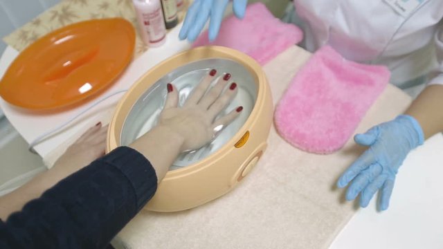 In a beauty salon, a girl dips her right hand into molten paraffin. Spa treatments.