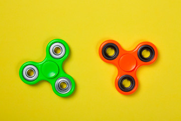 Orange and green fidget spinners close up stress relieving toys on yellow background.