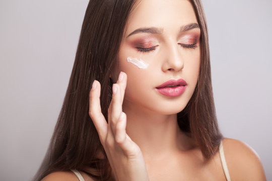 Woman with healthy face applying cosmetic cream under the eyes