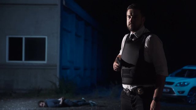 Wide portrait of an effective police officer wearing bullet proof vest while looking at camera after catching a suspect in the suburbs at night