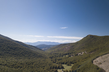 Aerial view of a beautiful mountain landscape, with hills full of green trees and a  small valley. Autumn season in Italy.