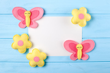 Craft pink and yellow butterfly and flowers with white paper, copyspace on blue wooden background. Hand made felt toys. Abstract sky.