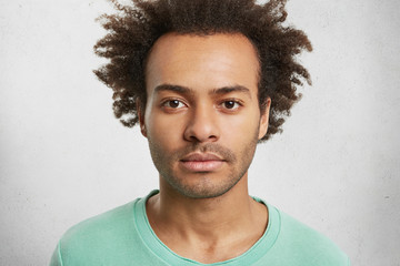 Portrait of dark skinned confident man with curly Afro hairstyle has calm face expression, looks...