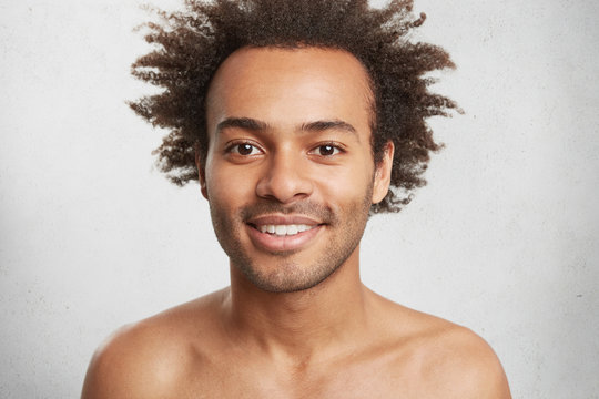 Naked positive Afro American male with dark healthy skin and curly hair, smiles gently as being glad after date with grifriend. Successful teenager pleased to hear pleasant news. People, lifestyle