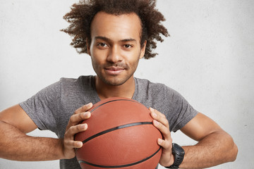 Dark skinned mixed race male advertises basketball. Handsome attractive unshaven male player waits for friends to play energetic game outdoor, spends weekends actively. Sport and lifestyle concept