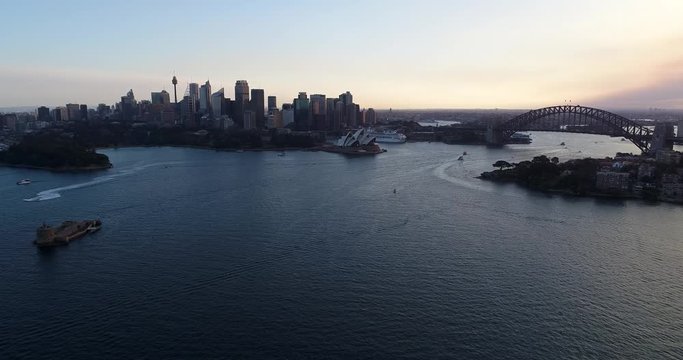 Above Sydney harbour towards main city landmarks – CBD high-rises and the Sydney Harbour bridge at sunset.

