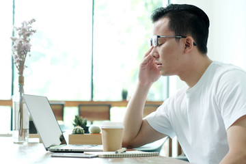 Young asian man get tired while working with laptop computer at casual office, business situation, emotional in office life