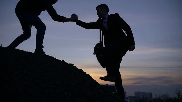 Businessman silhouette gived hand for pull team to peak mountain work together
