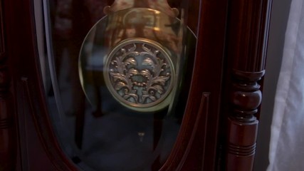 Decorative pendulum on a grandfather clock swinging back and forth.