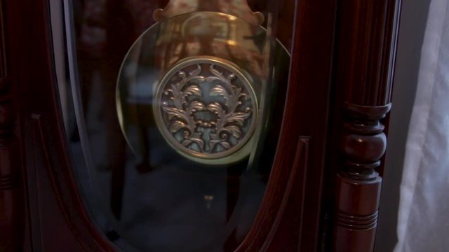 Decorative pendulum on a grandfather clock swinging back and forth.