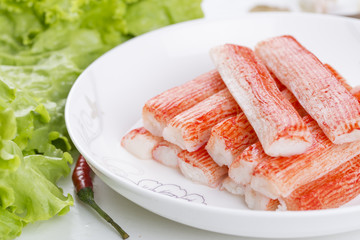 Red crab stick in a white plate. And green lettuce and coriander, pepper and other spices. 