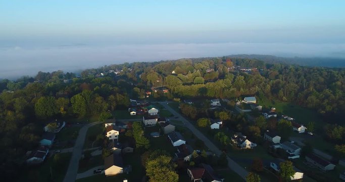 An early foggy autumn morning establishing shot over a typical New England residential neighborhood.  	