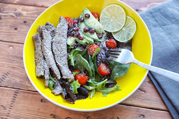 Salad with tomato and baby lettuce in yellow bowl.