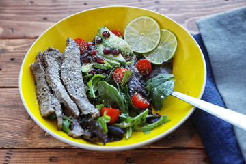 Salad with tomato and baby lettuce in yellow bowl.
