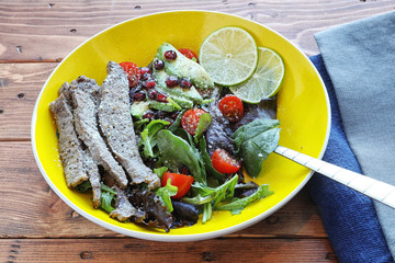 Salad with tomato and baby lettuce in yellow bowl.
