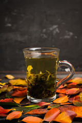 Cup of tea with autumn leaves, nuts, berries and spices on the rustic background. Shallow depth of field.