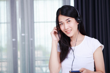 woman in headphones listening to music from smartphone with window background