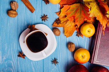 Maple leaves with a book and black coffee in a cup on a blue woo