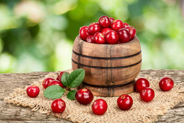 Cranberry with leaf in wooden bowl on old wooden table with blurry garden background