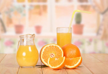 Jug and glass of fresh orange juice with straw, orange, half and slices on the kitchen background.