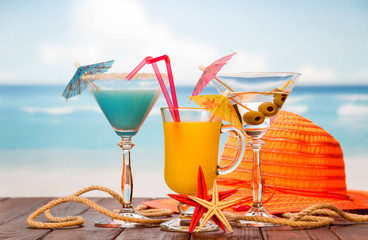 Cocktail, glass of orange juice and alcohol with olives, hat, starfish and twine on the background of the sea.