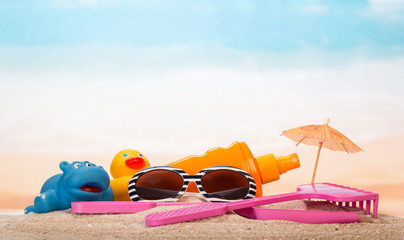 Sunscreen, sunglasses, umbrella and children's toys in the sand on the background of sea.