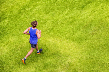 Fototapeta na wymiar Runner man running jogging on summer green grass texture park jogging healthy lifestyle. People working out cardio top view. Copy space on background.