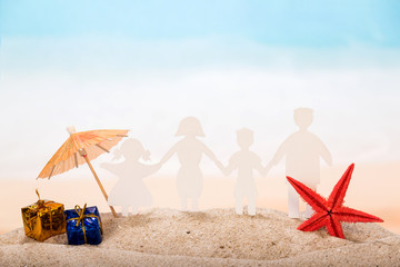 Fototapeta na wymiar Paper figures joined hands - family, an umbrella, gifts and starfish in the sand against the background of the sea.