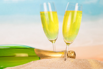 Bottle and two glasses with champagne in the sand against the background of sea.
