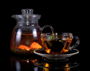 Cup of hot tea with a saucer and jug isolated on black background